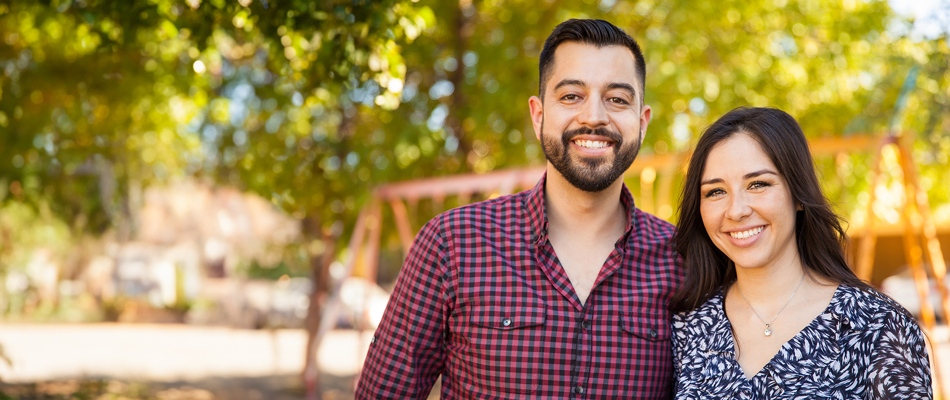 A man and a woman standing together outdoors, smiling at the camera.